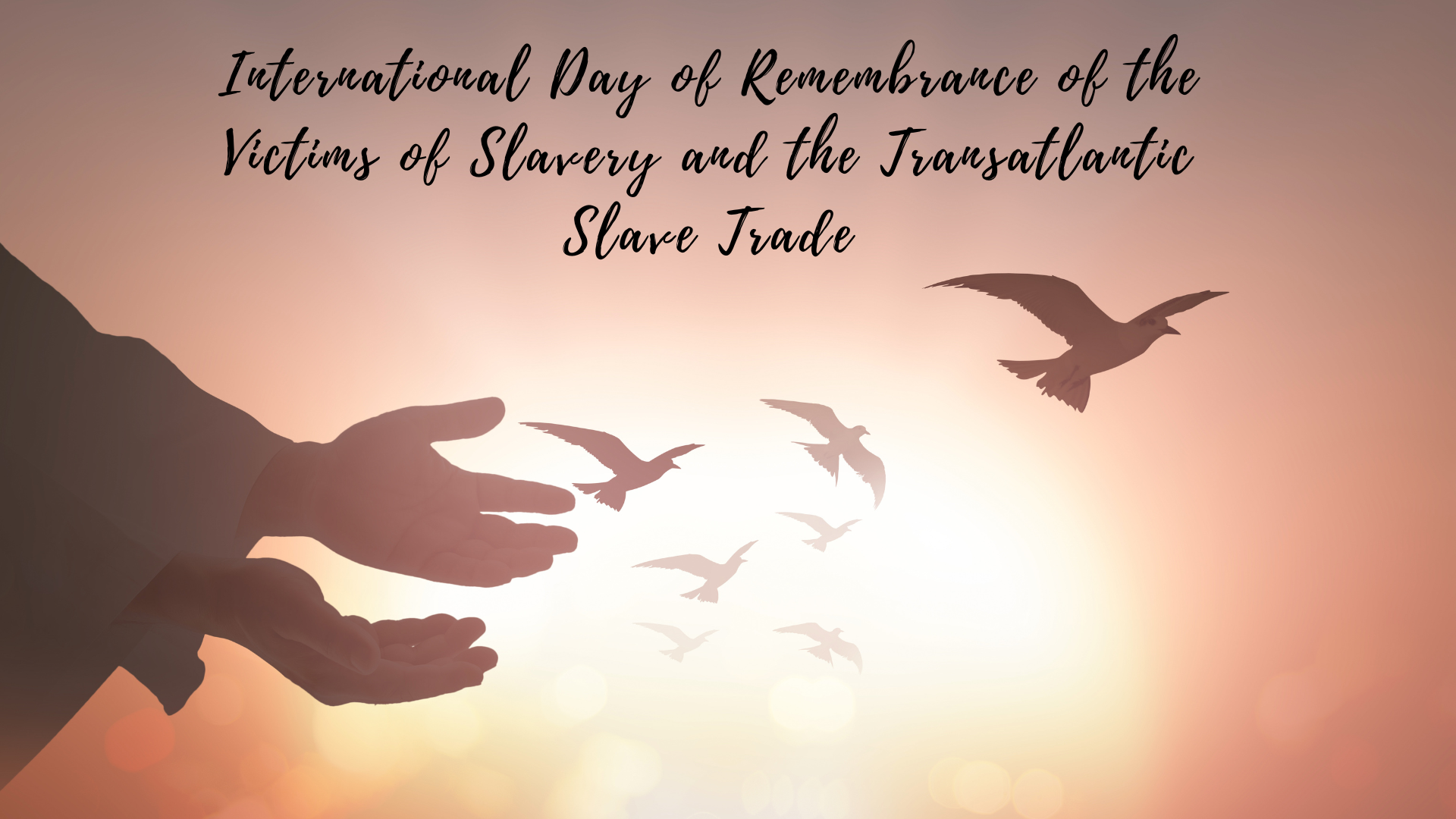 Commemorating the international day of remembrance of the victims of slavery and the transatlantic slave trade with open hands releasing doves into a sunset.