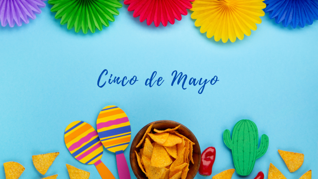 Vibrant cinco de mayo celebration setup with colorful paper fans, maracas, a cactus decoration, and a bowl of nachos on a blue background.