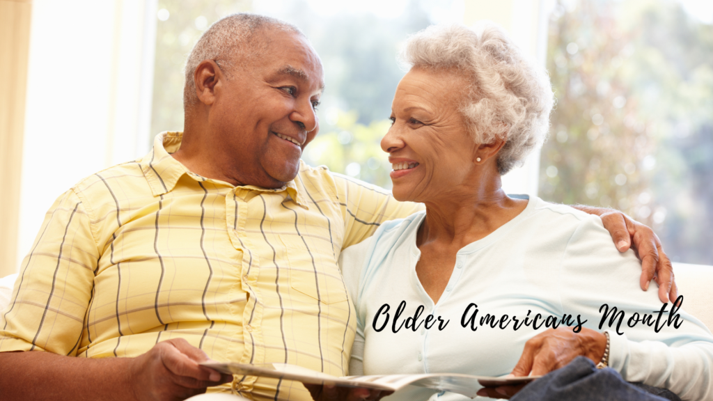 Senior couple smiling and embracing while looking at each other, with a gentle sunlight streaming through a window behind. text overlay: "older americans month.